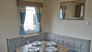 Un coin repas avec une table ronde dressée pour quatre personnes, un banc avec des coussins bleus et un miroir au mur.