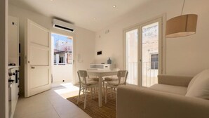 A modern living room with a sofa, a dining table with chairs, and a kitchen area visible through an open door. - Maruzza Home 101 (Favignana)