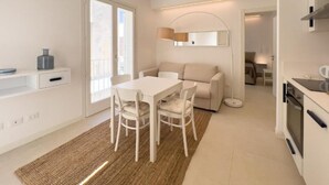 A modern kitchen with white cabinetry, a dining area with a white table and chairs, and a cozy living space with a sofa and a lamp. - Maruzza Home 101 (Favignana)