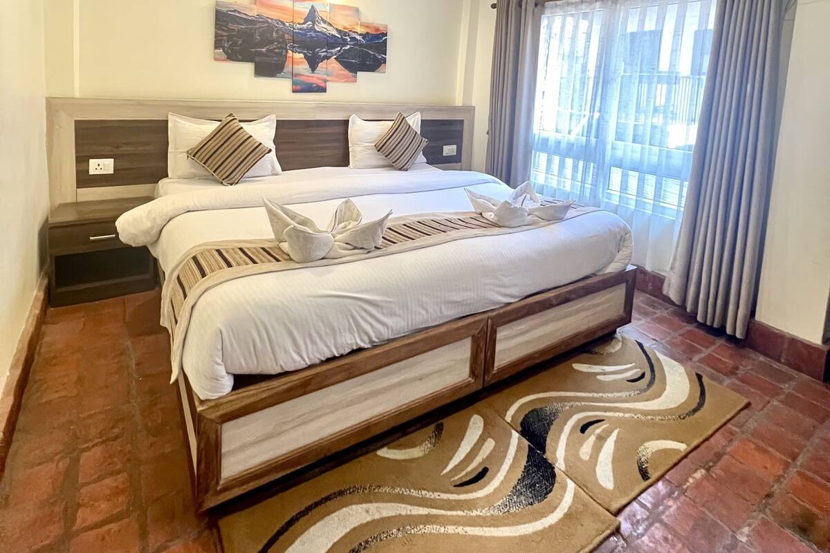 Un dormitorio moderno con una cama grande, un cabecero con una pintura, un techo con vigas de madera y una ventana con cortinas.