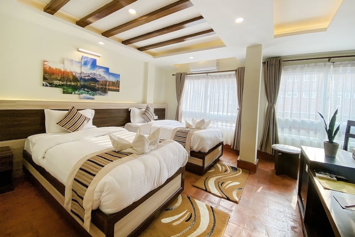 Una habitación de hotel con una cama grande, dos camas individuales, un escritorio y una ventana con cortinas.