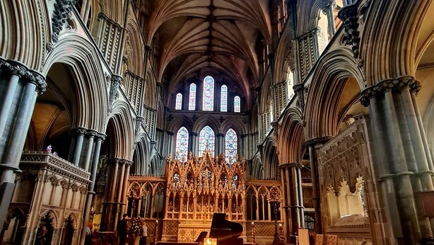 Interior de una catedral con suelo a cuadros, hileras de sillas y un órgano imponente.