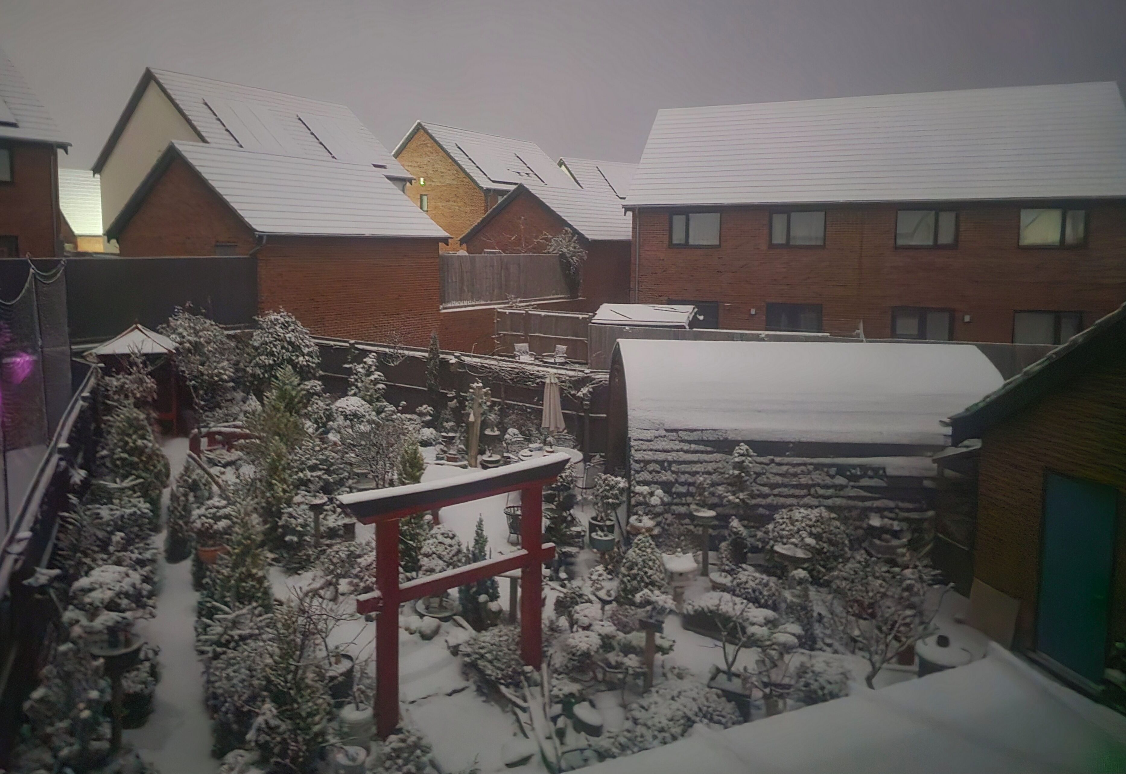A residential area with multiple houses, some with snow-covered roofs and a red torii gate in the foreground.