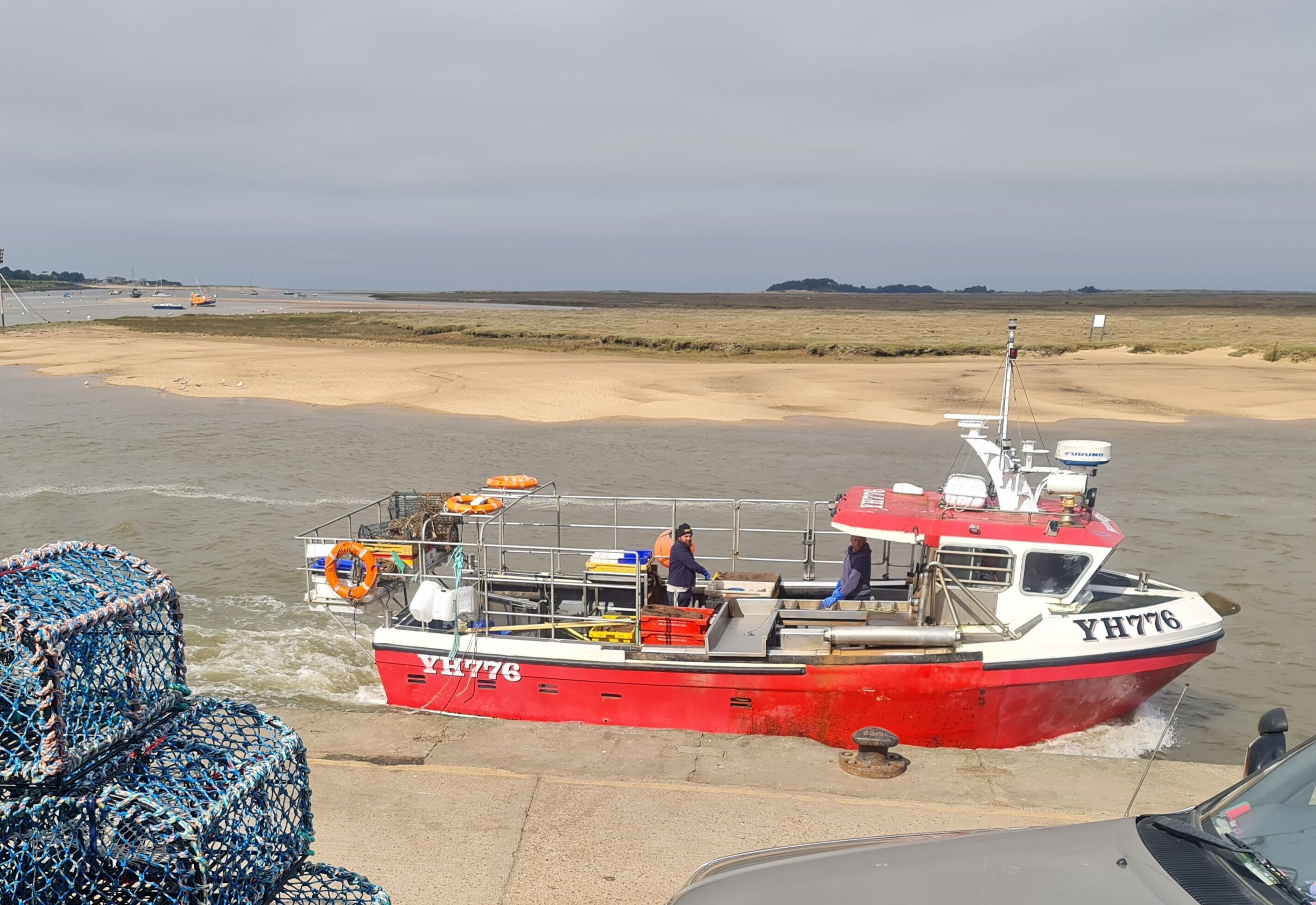 A red and white boat with the number YH776 docked at a sandy beach.