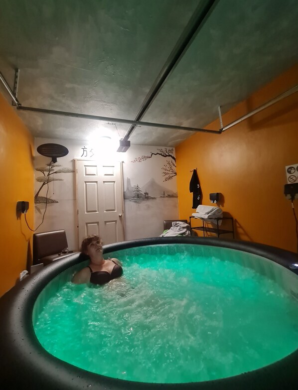 Une pièce avec un jacuzzi, une porte, un mur orné d’une fresque et un fauteuil.