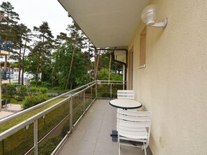 Relax on the balcony with a view of the well-maintained garden and surrounding trees, featuring a small table and two chairs.