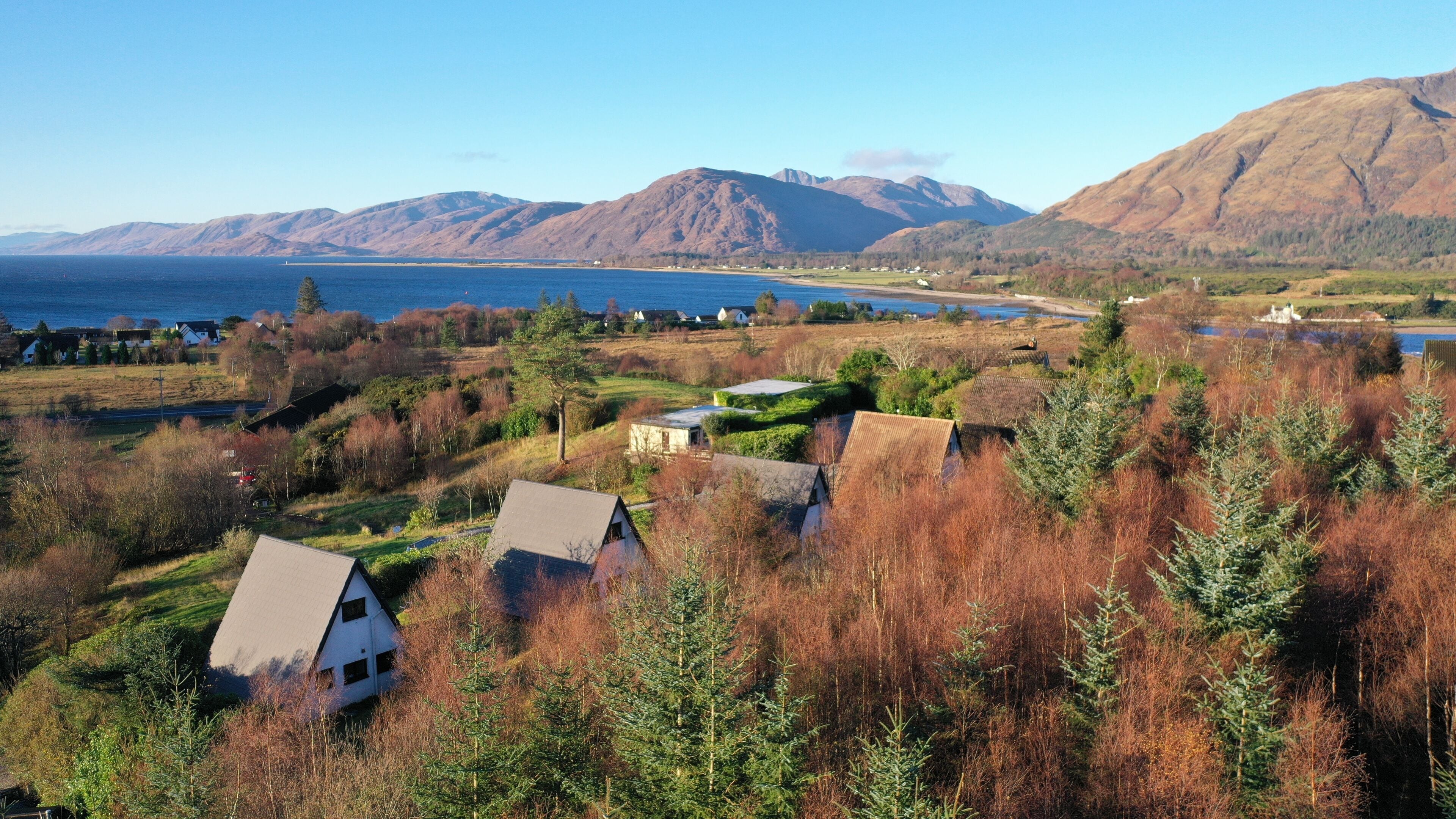 A coastal village with houses surrounded by trees and mountains in the background.