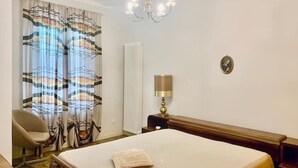 A hotel room with a bed, a chair, a lamp, a radiator, and a chandelier. - Apartment in the countryside (Piemonte)
