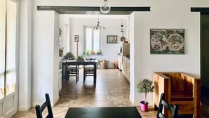 A dining area with a wooden table and chairs, a hanging light fixture, and a view into the kitchen. - Apartment in the countryside (Piemonte)