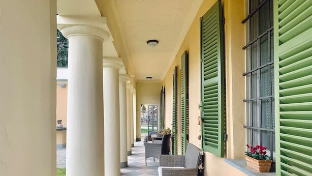 A covered corridor with columns, green shutters, and outdoor seating. - Apartment in the countryside (Piemonte)