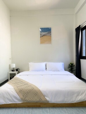 A neatly made bed with white linens, a small bedside table with a lamp, and a wall-mounted painting of a beach scene. - MONTANA Hotel & Hostel Phuket (Karon)