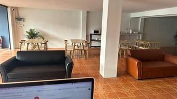 Amplia sala de estar con un sofá de cuero negro, un sofá de cuero marrón y una mesa de comedor con sillas. Hay una planta en maceta y un pilar blanco en el centro.