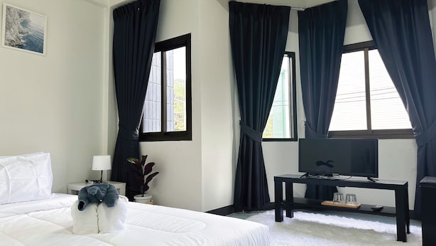 A hotel room with a bed, a desk with a TV, and large windows with dark curtains. - MONTANA Hotel & Hostel Phuket (Karon)