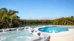 A hot tub and a pool with a view of a lake and palm trees. - Canal-Front Retreat w/ Pool, Hot Tub & Kayaks to Nature Preserve! 🛶 (Cocoa Beach)