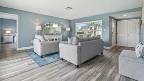 A spacious living room with a grey sofa set, a coffee table, and a patterned rug. - Canal-Front Retreat w/ Pool, Hot Tub & Kayaks to Nature Preserve! 🛶 (Cocoa Beach)