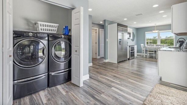 A modern kitchen with stainless steel appliances, a dining area with a table and chairs, and a laundry room with two washing machines. - Canal-Front Retreat w/ Pool, Hot Tub & Kayaks to Nature Preserve! 🛶 (Cocoa Beach)