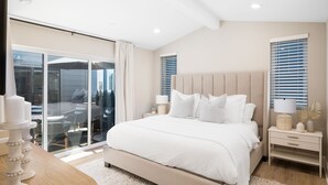 Un dormitorio moderno con una cama grande, un vidrio que da a un balcón y una mesita de noche con lámpara.