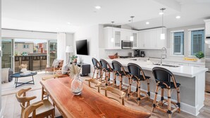 Una cocina moderna con armarios blancos, una isla central con taburetes y una zona de comedor con mesa y sillas de madera.