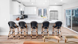 Una cocina moderna con armarios blancos, una isla central con taburetes y un amplio ventanal que proporciona luz natural.