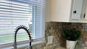 A kitchen with a stainless steel sink, a window with blinds, and a potted plant. - Great First Floor Condo! (Greenville)