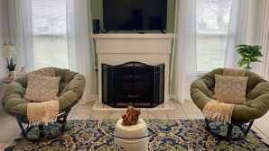 A living room with two green armchairs, a fireplace, and a TV on a mantel. - Great First Floor Condo! (Greenville)