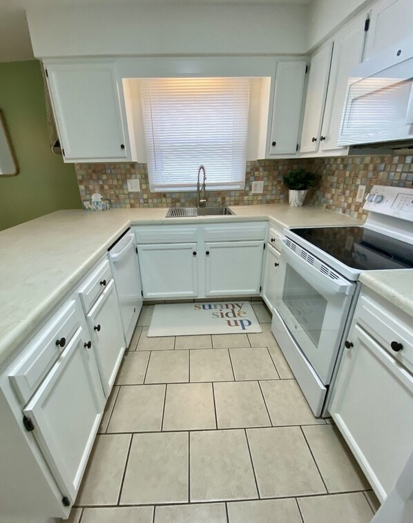 A compact kitchen with white cabinets, a double sink, a stove, and a tiled backsplash.