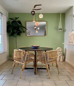 A dining area with a round table, four wicker chairs, a mirror, and a hanging light fixture.