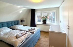 A bedroom with two beds, a window with a view, a radiator, and a cabinet.