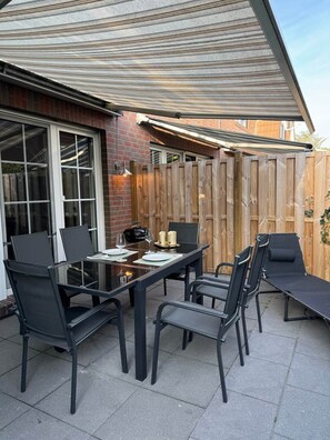 An outdoor patio with a table and chairs, a wooden fence, and a brick wall.