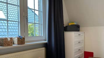 Ein Kinderzimmer mit Fenster, Heizkörper, einer weißen Kommode und einer Spielmatte.