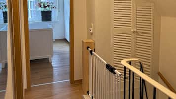 Eine Holztreppe mit weißer Geländer führt zu einem Raum mit Heizkörper und einem Fenster mit Vorhängen.