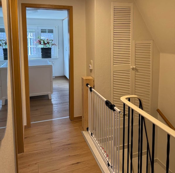 A wooden staircase with a white railing leading to a room with a radiator and a window with curtains. - Maila Vacation Home (Varel)