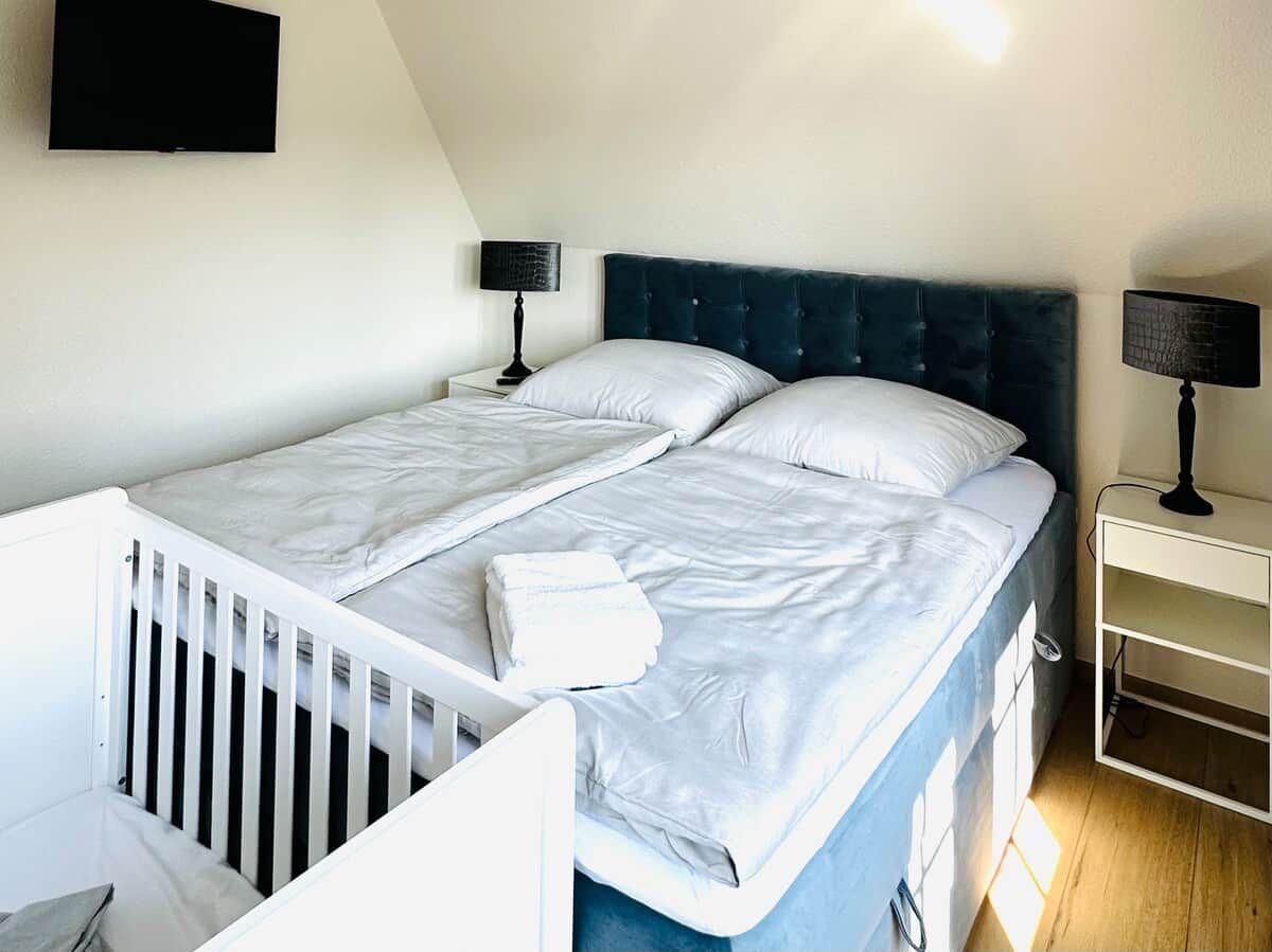 A bedroom with a bed, two bedside tables, and a TV mounted on the wall.