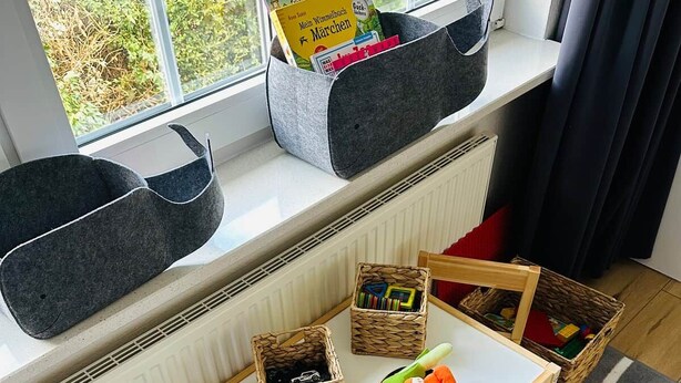 A child's play area with a table, chairs, and storage baskets on a window sill.