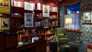 A cozy reading room with bookshelves, a green armchair, and a small round table. - Beaverbrook Town House (London)