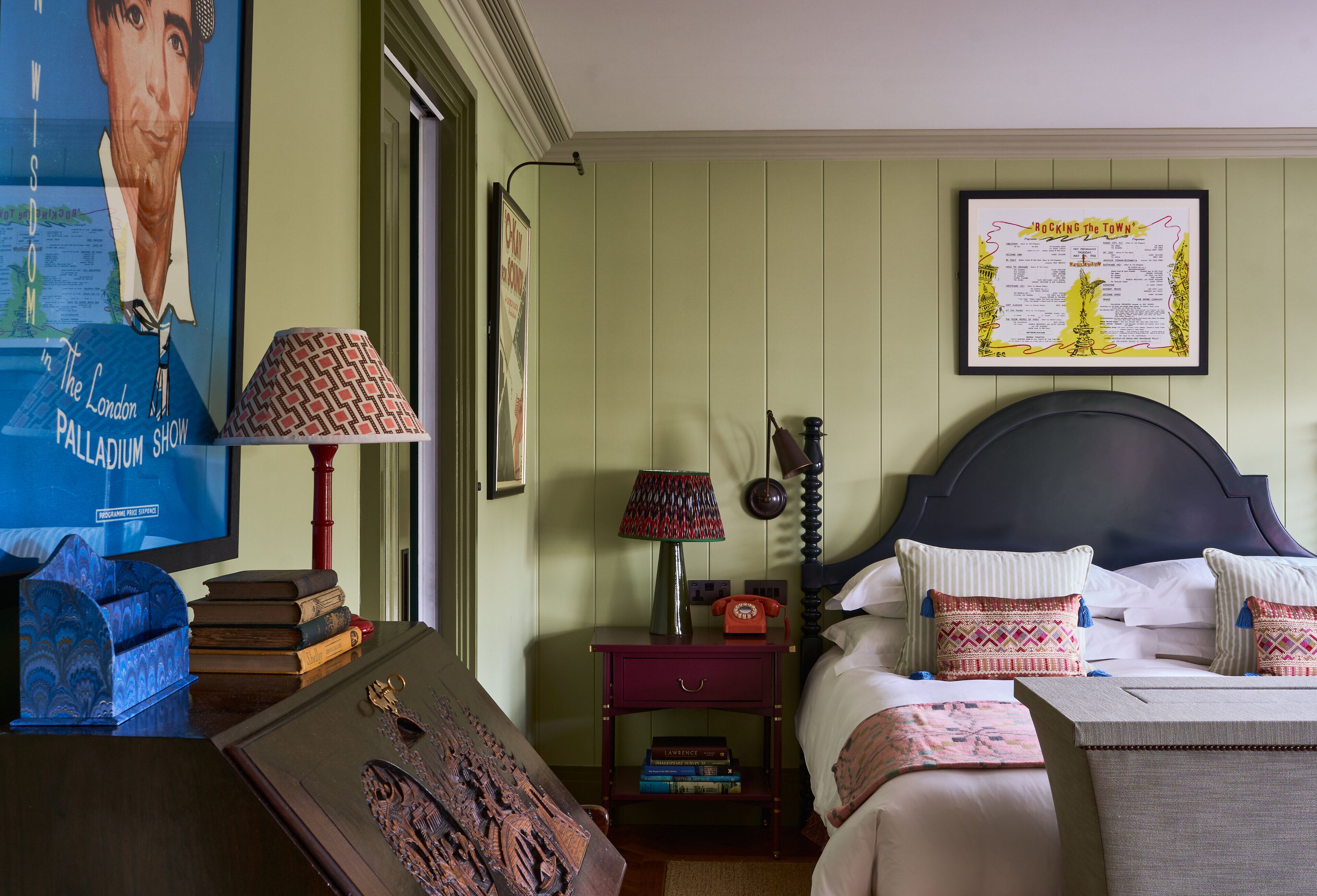 A room with a bed, a nightstand with a lamp, a framed poster on the wall, and a bookshelf with books.