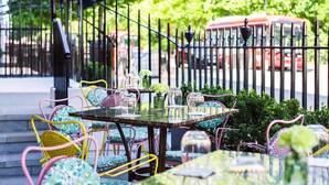 An outdoor dining area with a table set for two, surrounded by colorful chairs, a decorative glass vase, and a metal fence. - Beaverbrook Town House (London)