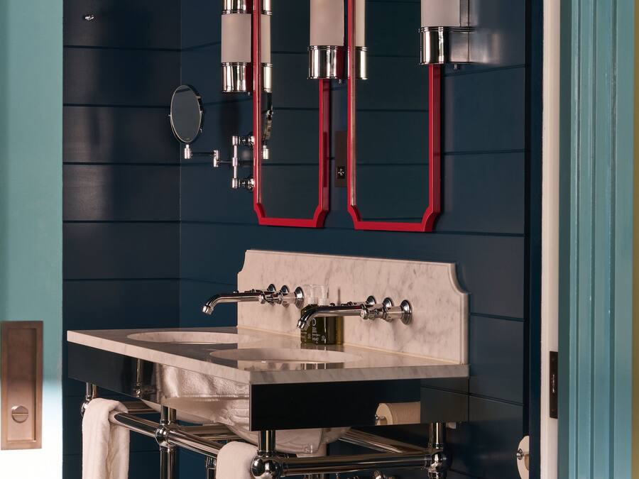 A modern bathroom with a dark blue wall, a marble sink, chrome fixtures, and two mirrors with red frames.