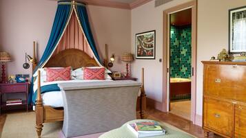 A bedroom with a four-poster bed, a wooden dresser, and a green ottoman.