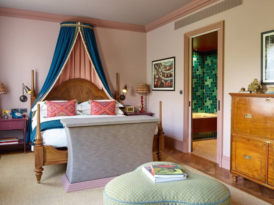 A bedroom with a four-poster bed, a wooden dresser, and a green ottoman.