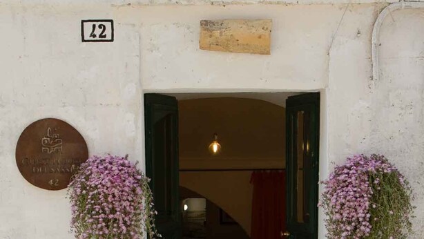 A building entrance with a door, a plaque, and hanging flower baskets. - Stay Matera 42 - apartment in the Sassi (Matera)