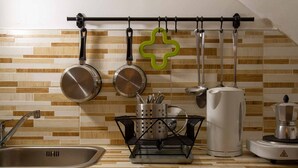 A kitchen with a wooden backsplash, hanging pots, a coffee maker, and a kettle on the counter. - Stay Matera 42 - apartment in the Sassi (Matera)