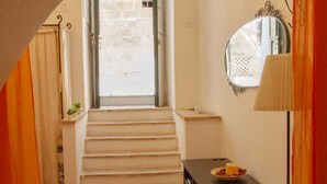 A staircase leading to a door with a view of a garden, a small table with a candle, and a lamp on the right. - Stay Matera 42 - apartment in the Sassi (Matera)