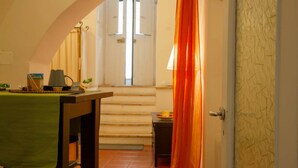 A narrow hallway with a staircase leading to a door with a window. A table with a lamp and a plant is visible in the foreground. - Stay Matera 42 - apartment in the Sassi (Matera)