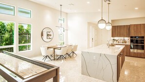 A modern kitchen with a marble island, wooden cabinets, and a dining area with a round table and chairs. - Indian Wells Luxury - Private Pool & Shuffleboard! (Indian Wells)