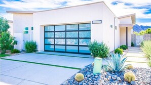 A modern two-story house with a large garage door, surrounded by a landscaped garden with cacti and shrubs. - Indian Wells Luxury - Private Pool & Shuffleboard! (Indian Wells)