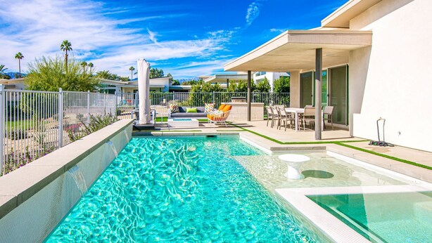 A swimming pool with a clear blue water, surrounded by a white fence and a covered seating area with chairs and a table. - Indian Wells Luxury - Private Pool & Shuffleboard! (Indian Wells)