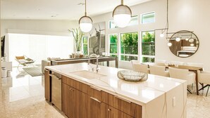 A modern kitchen with a central island, wooden cabinets, and pendant lighting. - Indian Wells Luxury - Private Pool & Shuffleboard! (Indian Wells)