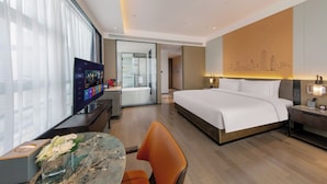 Una habitación de hotel moderna con una cama grande, un escritorio con una computadora, un televisor y un baño visible a través de una puerta abierta.