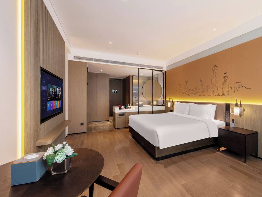 Una habitación de hotel moderna con una cama grande, mesitas de noche, un televisor y una obra de arte colgada en la pared.